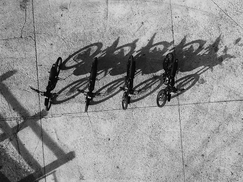 Ombres de motos et de pilotes projetées sur le gravier, en noir et blanc