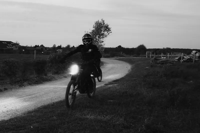 Un pilote, phare allumé, sur un chemin à la tombée de la nuit, en noir et blanc